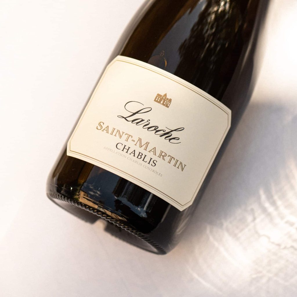 Bouteille de vin blanc Chablis Saint-Martin du Domaine Laroche, couchée sur une surface claire, symbolisant un éveil des papilles et une dégustation élégante.